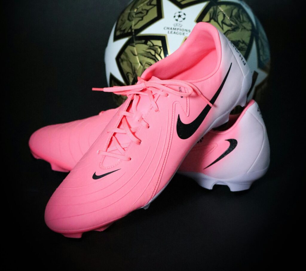 Bright pink soccer cleats paired with a Champions League ball on a dark backdrop.