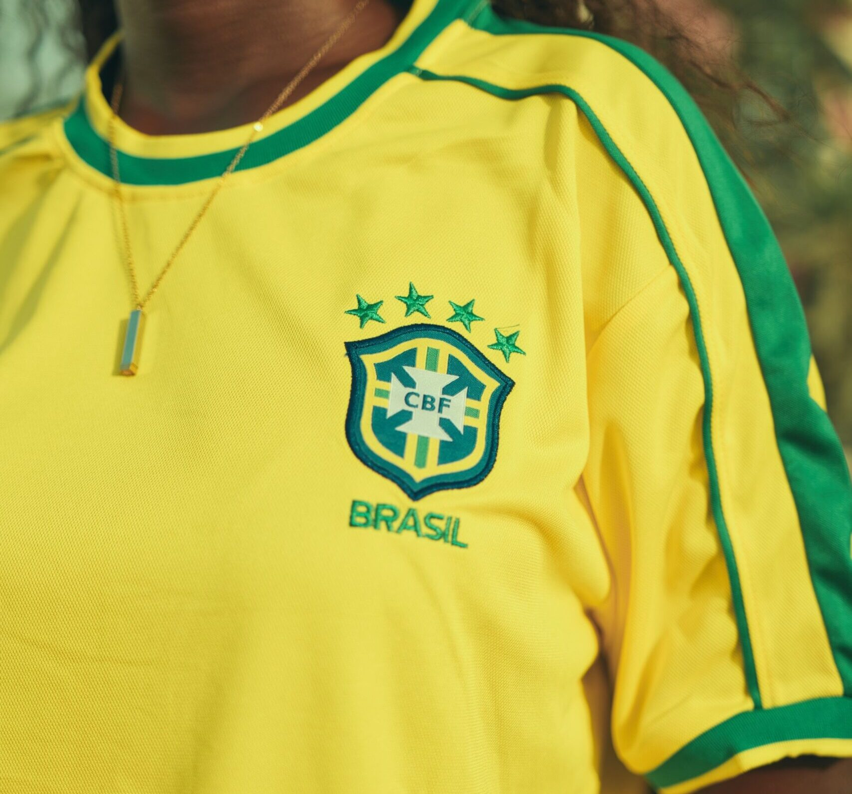Person wearing Brazilian soccer jersey with CBF logo in bright outdoor setting.